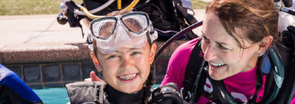 Instructor pointing out marine life to a student underwater.